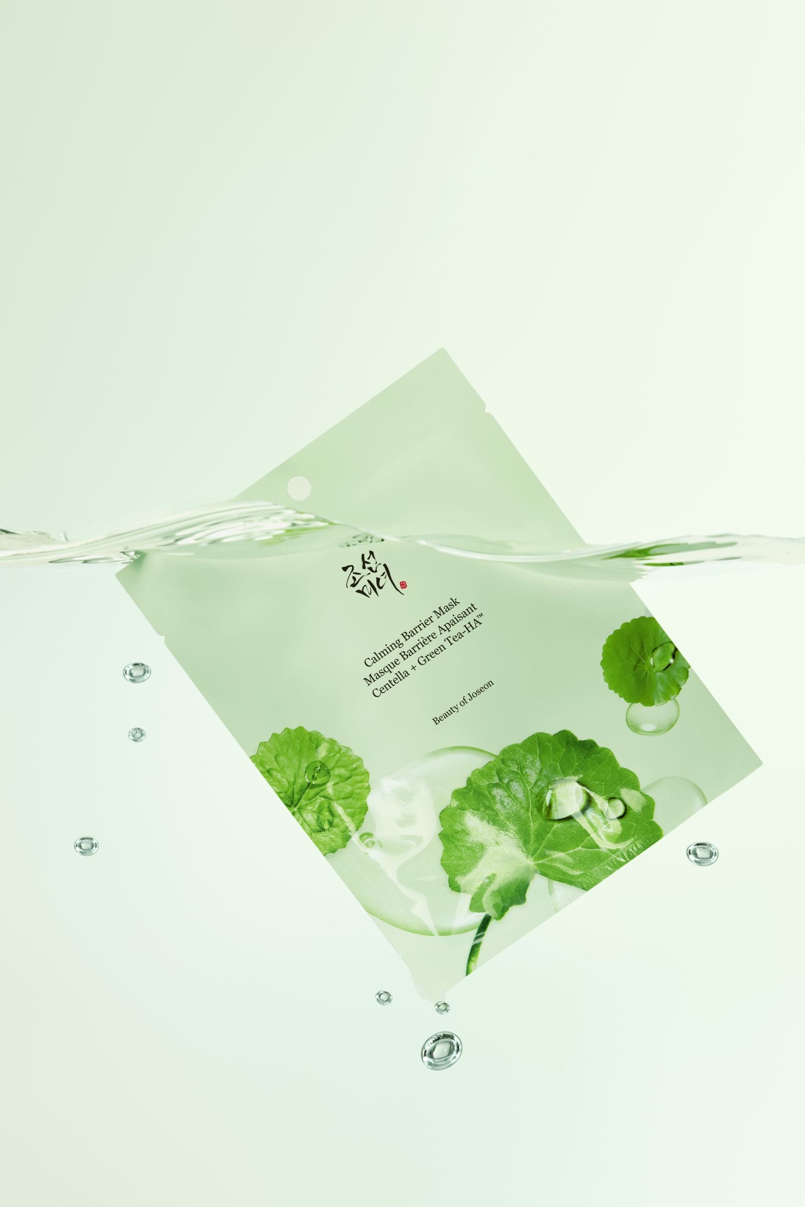 A single square sheet mask packet floating on water, printed with green leaf illustrations and text reading 'Calming Green Tea Mask' and 'Calming Green Tea Mask Sheet'.