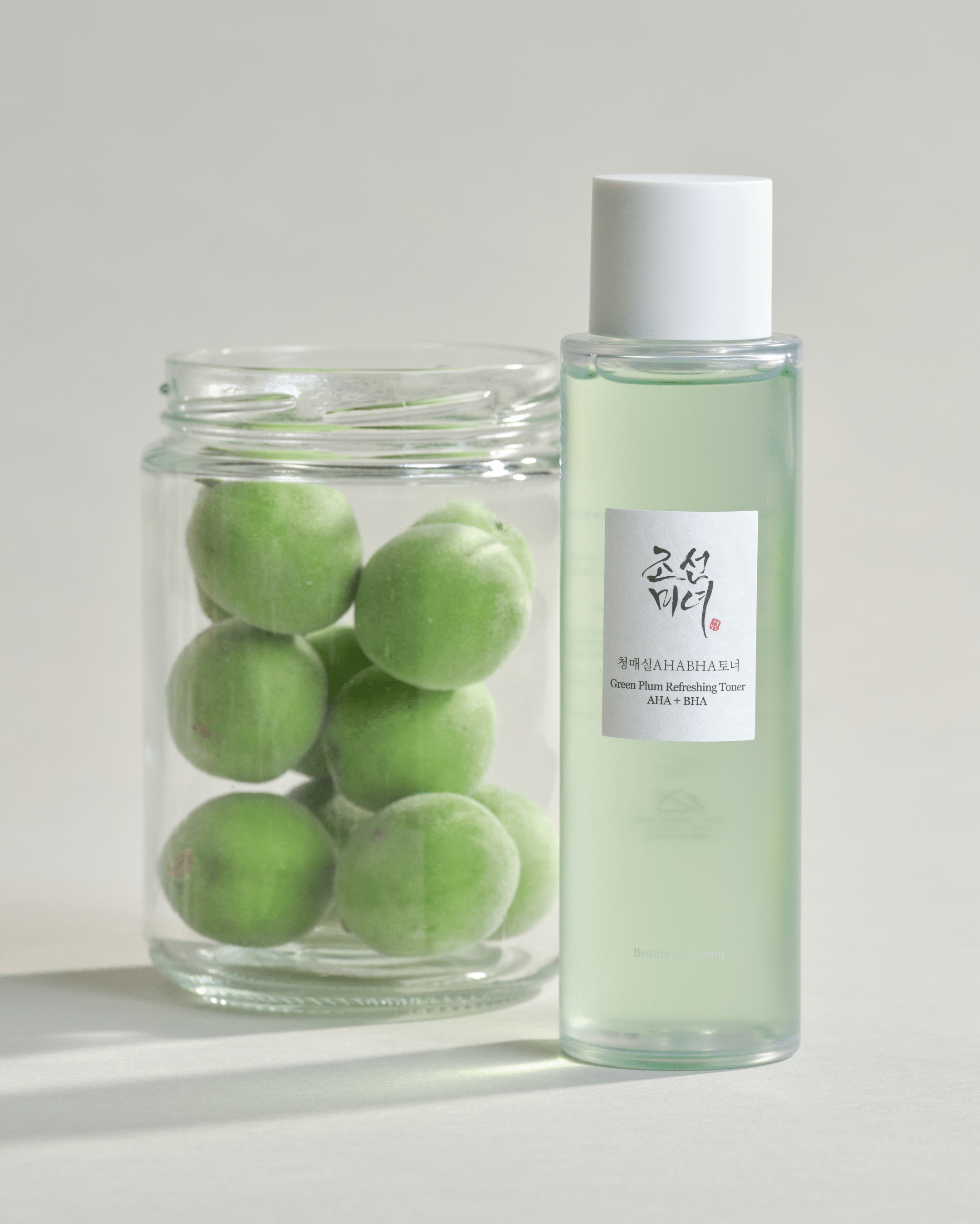 Green plum Refreshing Toner bottle next to a glass jar with green plums